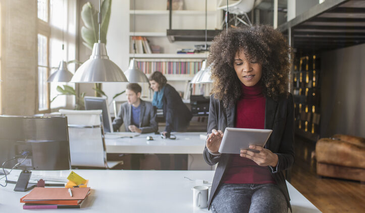 A Black Millenial worker reads from a tablet in a bright office. Can your knowledge management system mitigate the great resignation?