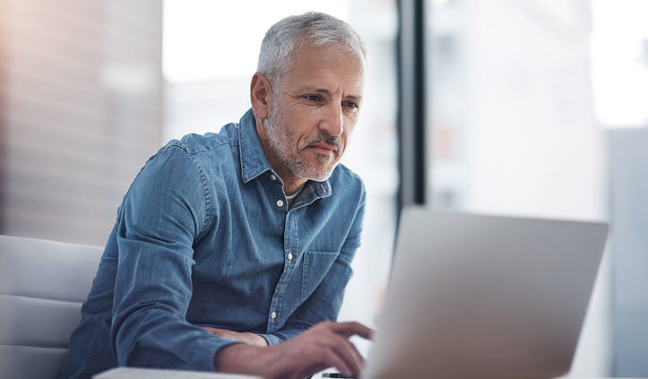 Middle aged man in denim shirt working on laptop. Market research is now called customer insights.