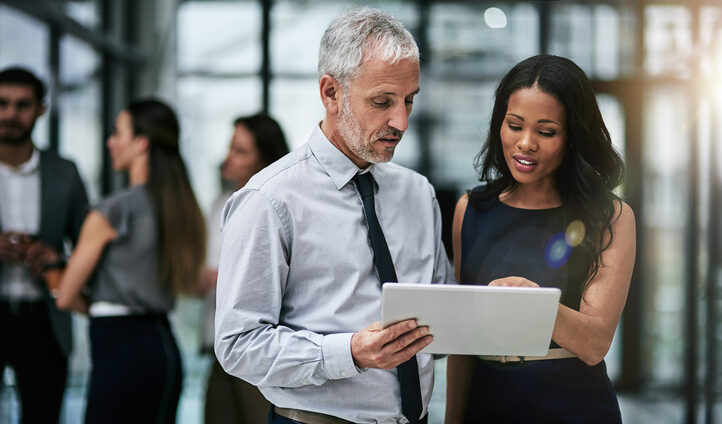 A middle aged man and a woman review a tablet screen. Measuring ROI of a competitive intelligence portal can be challenging.