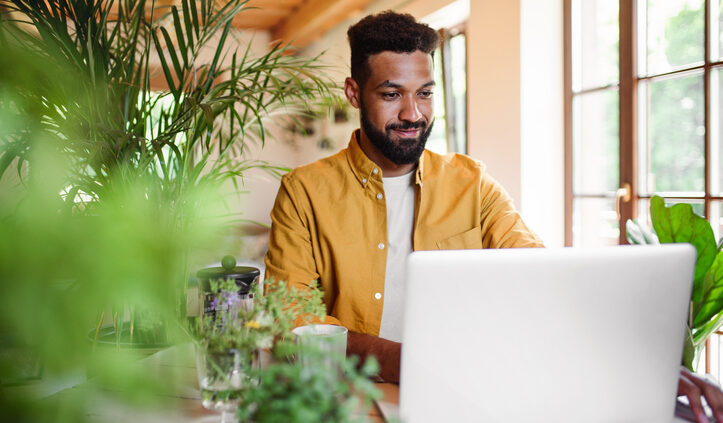 The decline in search skills means knowledge management systems must operate differently. A young man with laptop and coffee working indoors, home office concept.