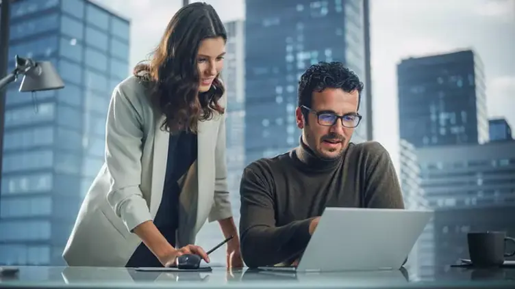 Two people discuss knowledge management while seated at a desk and looking at computer