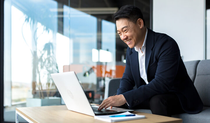 Senior Asian business man working on laptop online, smiling and rejoicing, happy boss business owner working in office. Competitive Intelligence portal