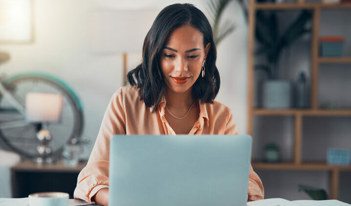 Woman working on laptop online, checking emails and planning on the internet while sitting in an office alone at work. Business woman, corporate professional or manager searching for competitive intelligence